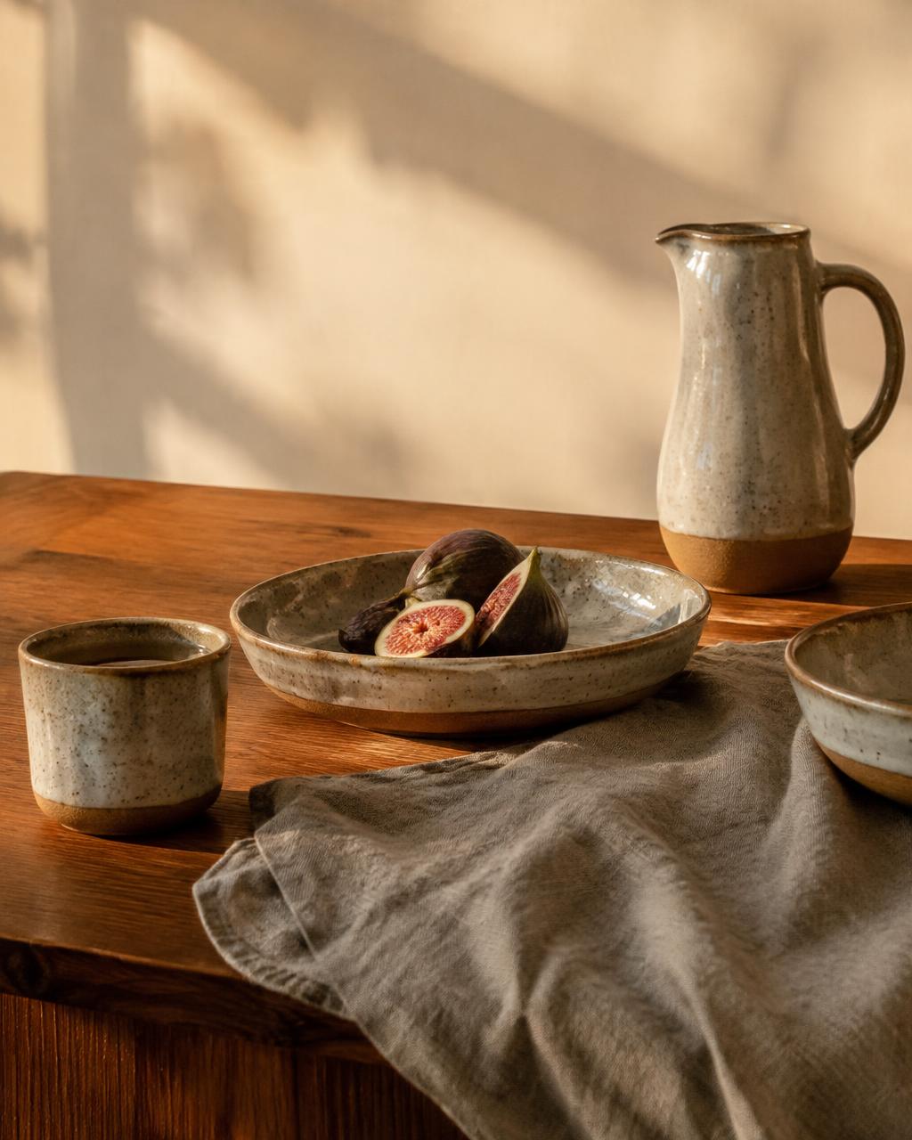 Detalhe de decoração: mesa de madeira, cerâmica, linho, luz de fim de tarde. Sem logótipos nem produtos identificáveis.